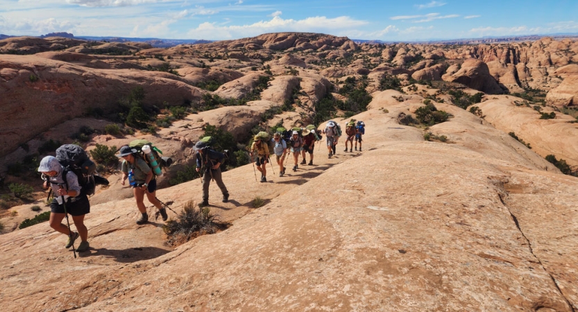 a group of backpackers make their way through a desert landscape on an outward bound course